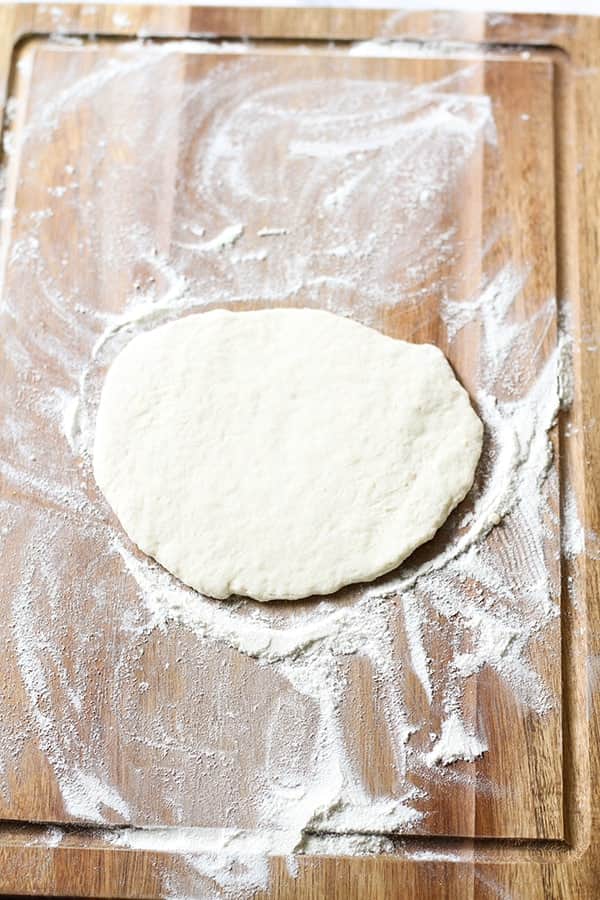 flattened pizza dough on a wooden cutting board.
