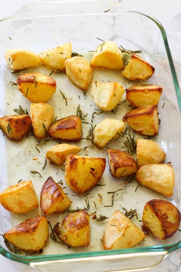 Golden potato pieces in a glass baking tray just out of the oven. 