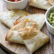 quesadilla quarters on a wooden board with avocado and salsa.