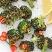 roasted broccoli on a white plate with lemon wedges and chopped chilli.