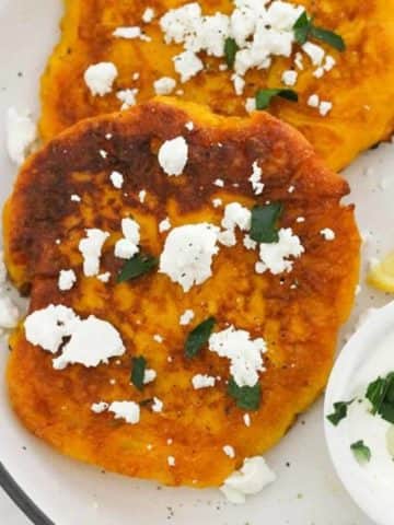 two fritters on a white plate topped with feta and parsley with text overlay "pumpkin fritters".