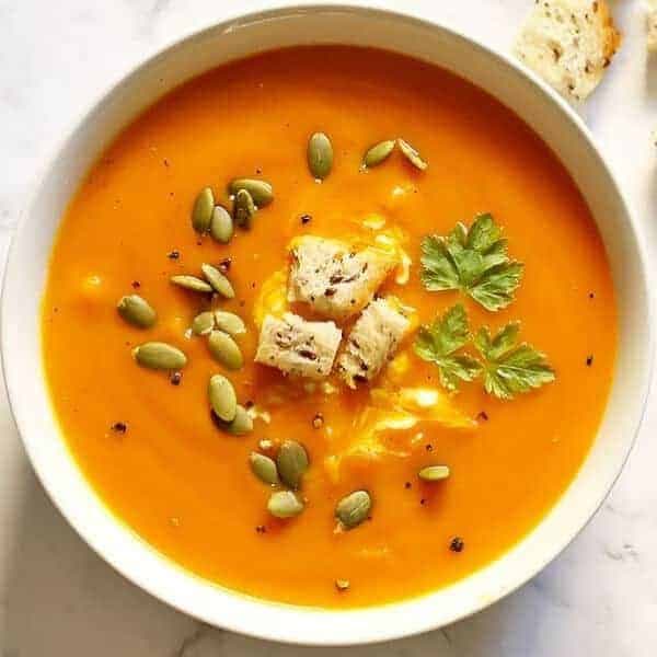a bowl of roasted pumpkin, sweet potato and carrot soup topped with croutons and pepitas