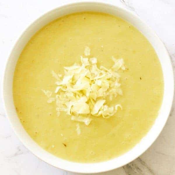 Potato and Leek Soup in a white bowl topped with shredded cheddar cheese.