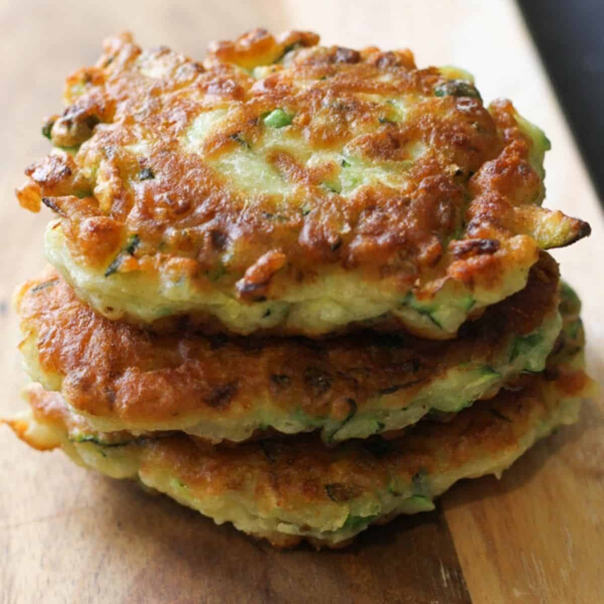 pea & feta fritters stacked on top of each other on a wooden serving board.