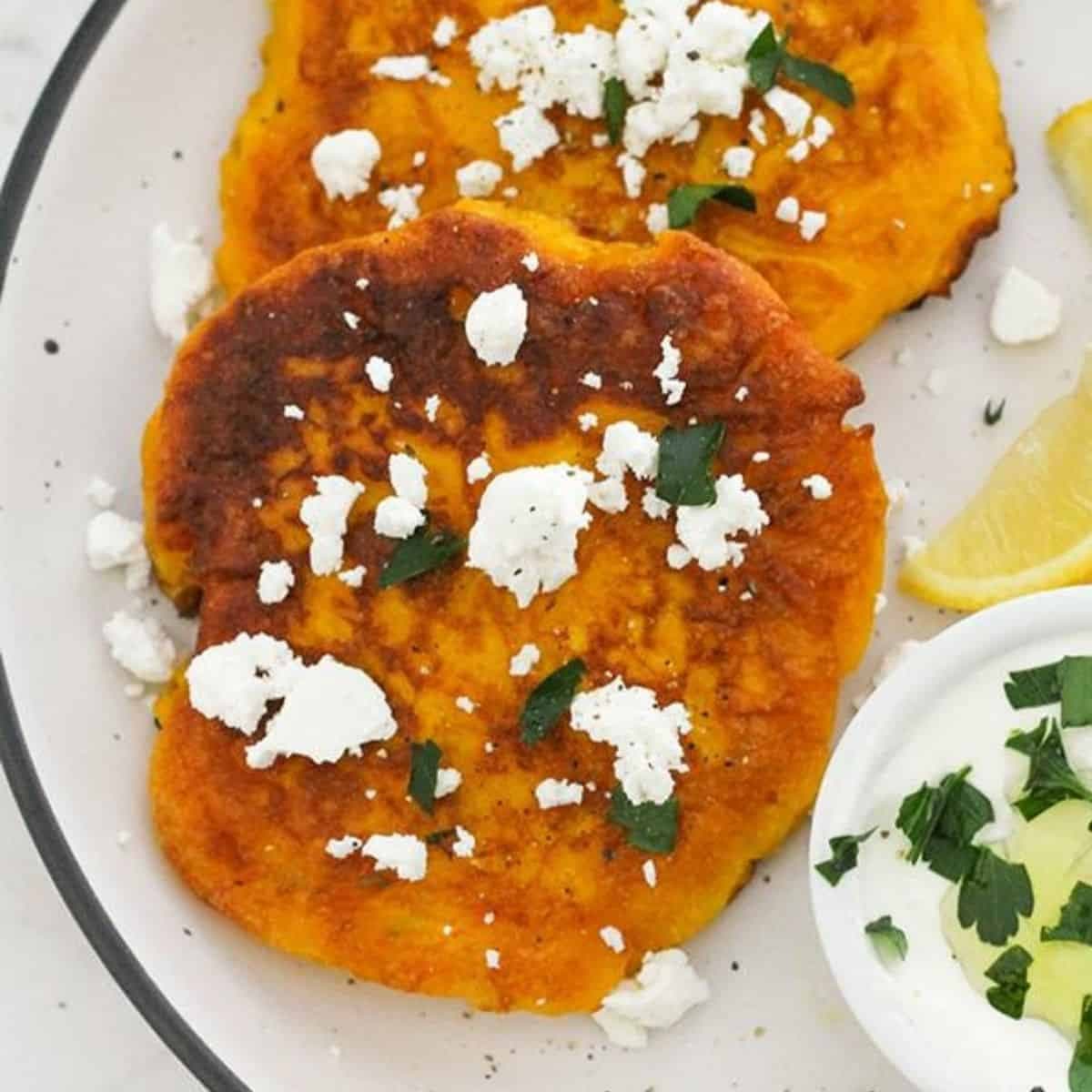 two fritters on a white plate topped with feta and parsley with text overlay "pumpkin fritters".