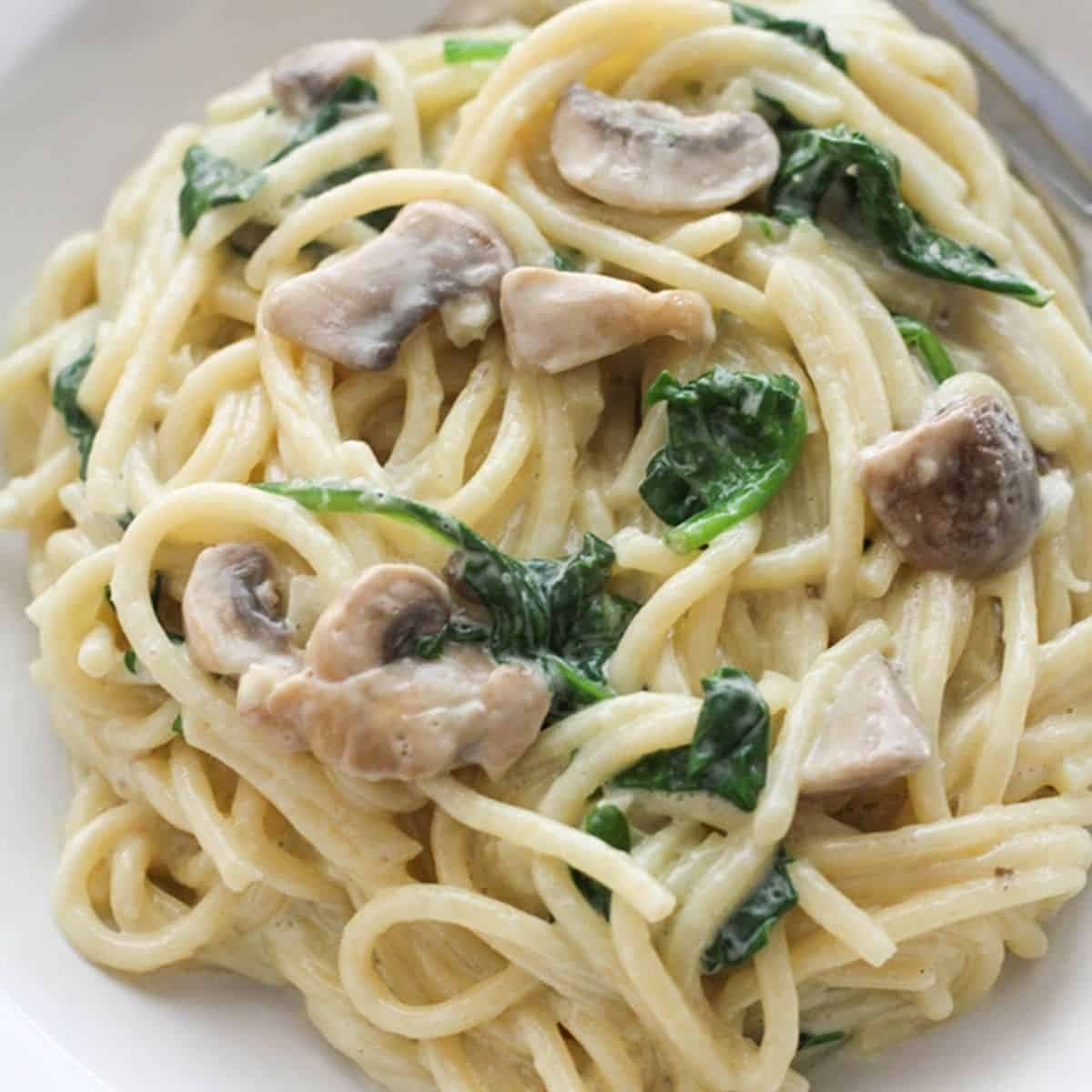 spinach and mushroom pasta in a white bowl.