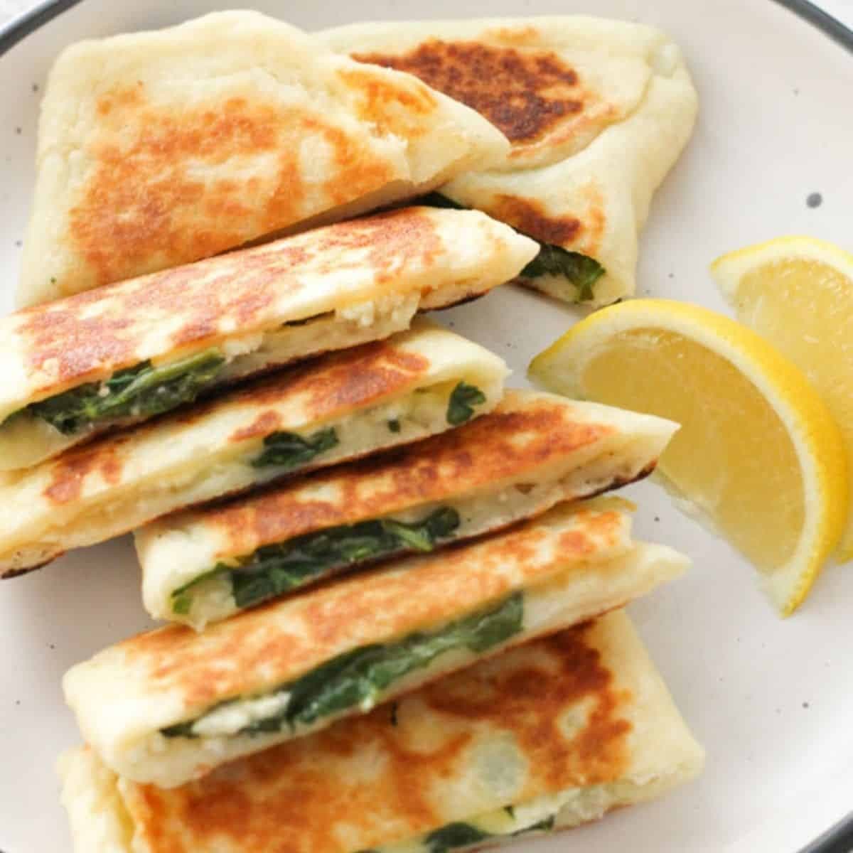 spinach and feta gozleme stacked on top of each other on a white plate.