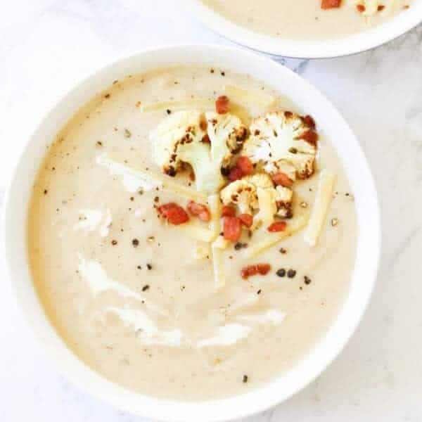 cauliflower and bacon soup in a white bowl topped with bacon bits and roasted cauliflower pieces