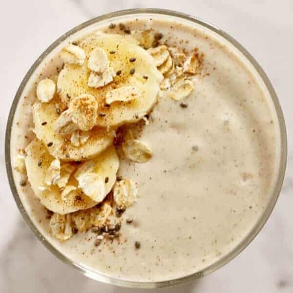 banana oat smoothie close up topped with banana slices, rolled oats, cinnamon and chia seeds