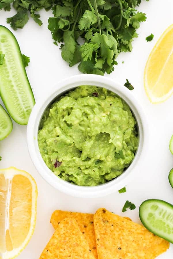 healthy guacamole in a white bowl surrounded by ingredients.