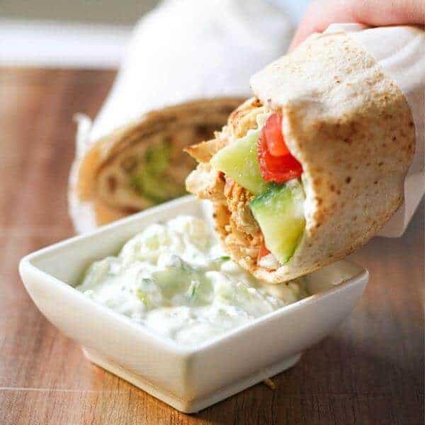 hand dipping a chicken gyro into a bowl of tzatziki sauce