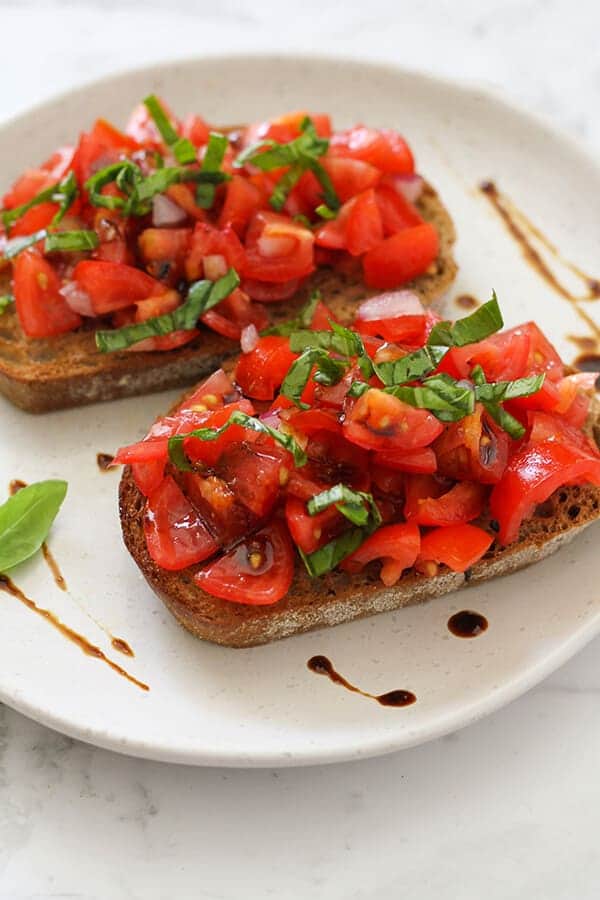 two pieces of brushetta on a white plate covered in balsamic glaze.