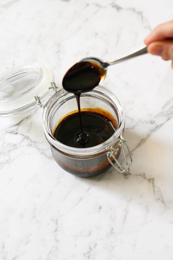 balsamic glaze in a glass jar with a spoon being held above it.