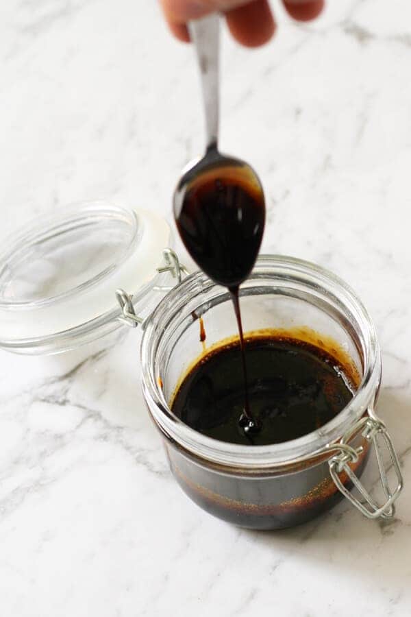 balsamic glaze in a glass jar with a spoon being held above it.