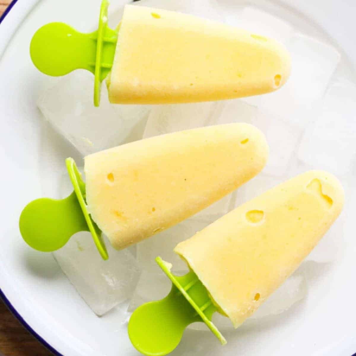 mango pineapple popsicles on a white plate covered in ice cubes.