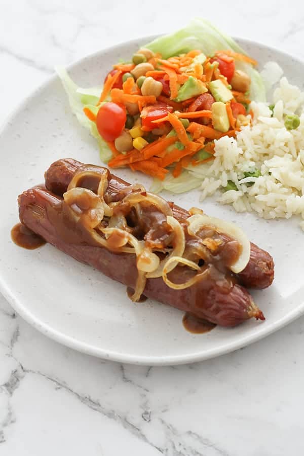 sausages on a plate covered in onions and gravy.