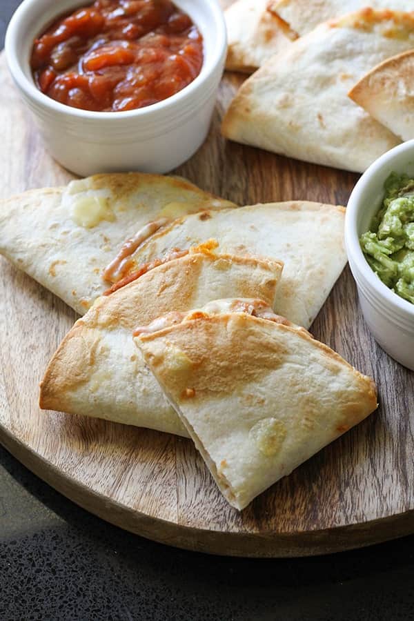quesadilla quarters on a wooden board with guacamole and salsa.