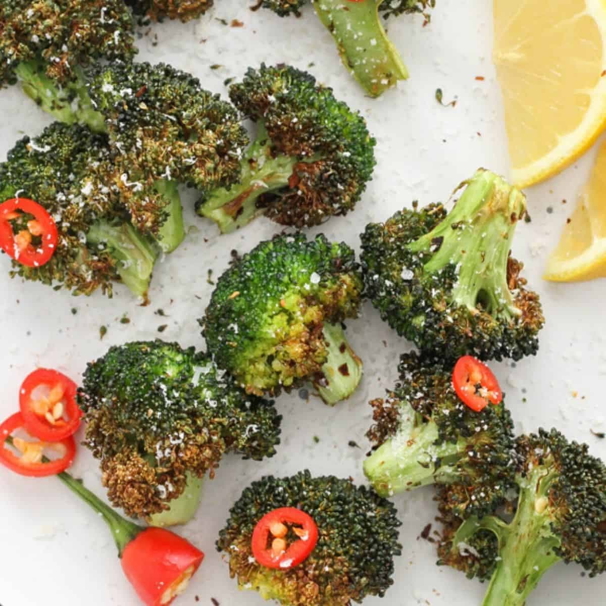 roasted broccoli on a white plate with lemon wedges and chopped chilli.