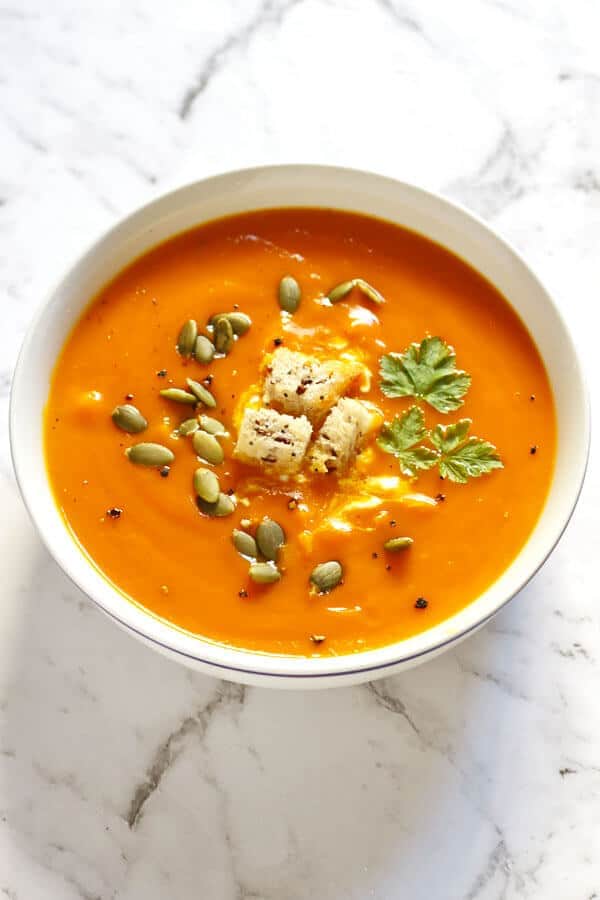 roasted pumpkin and sweet potato soup in a white bowl topped with seeds and croutons