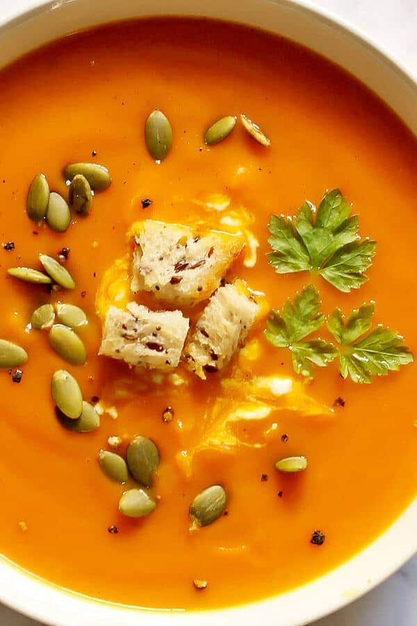 close up of a bowl of roasted pumpkin and sweet potato soup topped with seeds and croutons