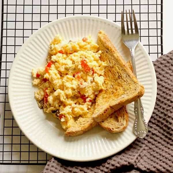 Easy scrambled eggs with veggies and two pieces of toast on a white plate