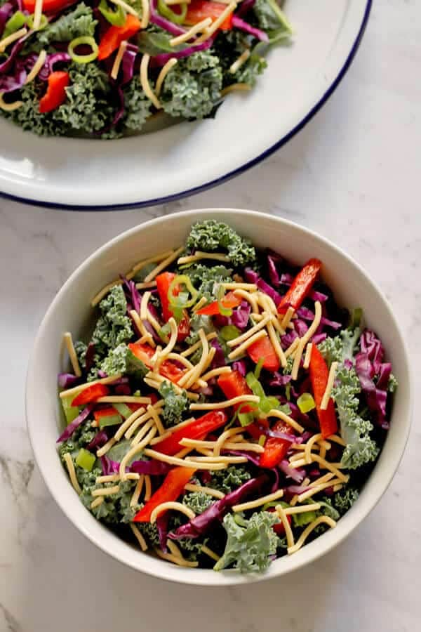 crunchy kale salad with lemon tamari dressing in a white bowl with a plate of salad in the top left corner