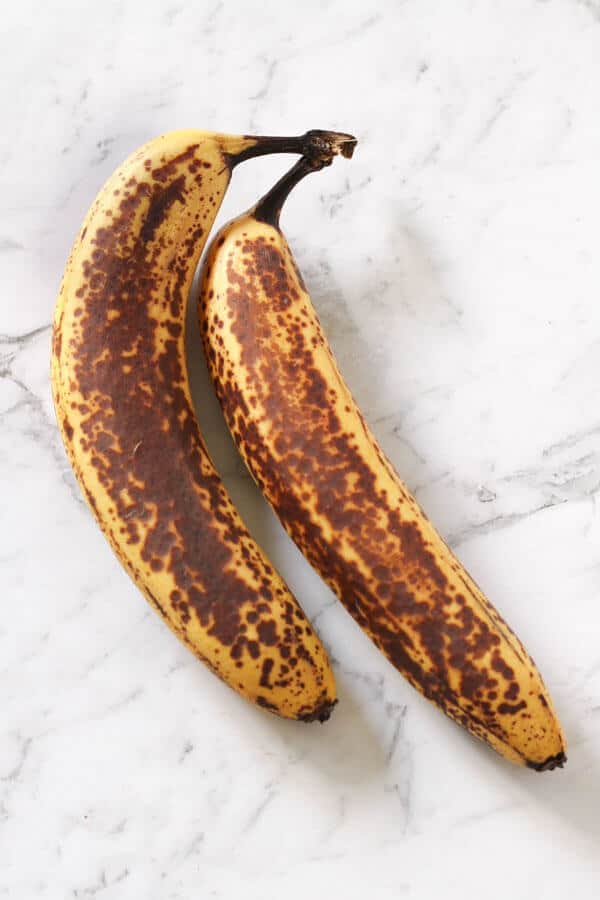 two spotty bananas on a white marble background