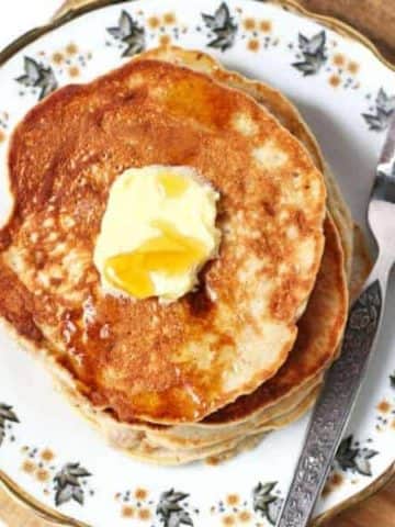 healthy banana pancakes stacked on a pattered plate with butter and maple syrup on top