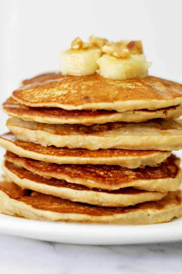 healthy banana pancakes stacked on a white plate with caramelised banana slices and pecans on top