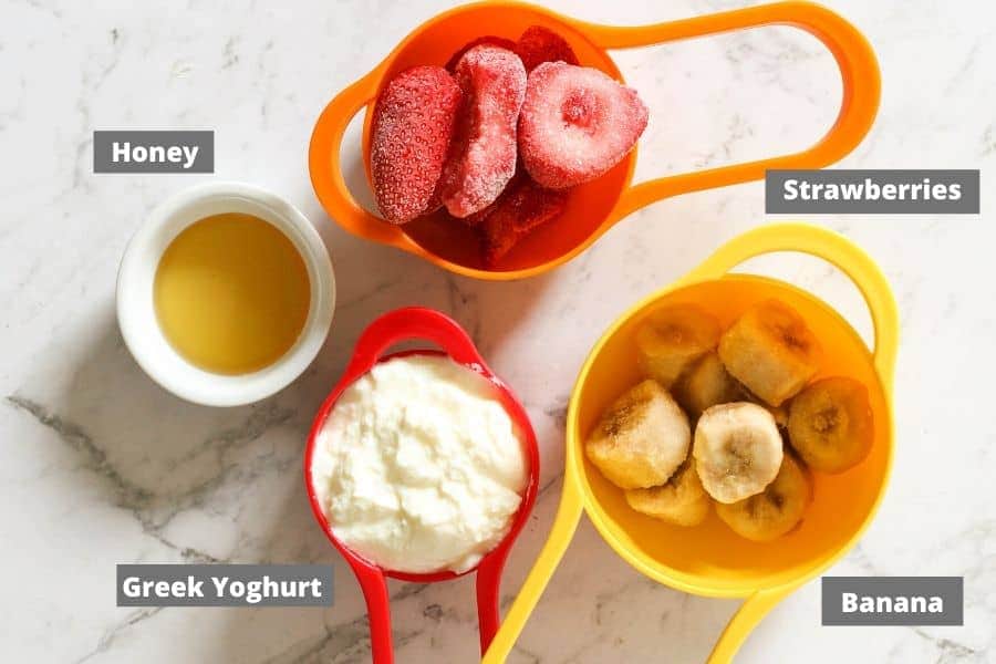 strawberry banana popsicle ingredients on a white marble background.