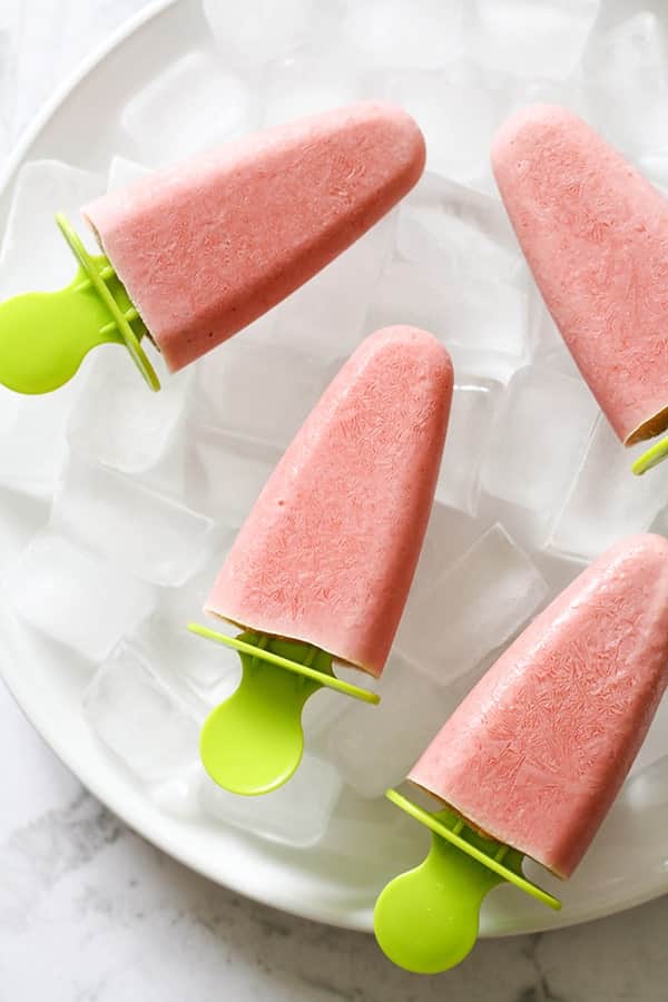 4 strawberry banana popsicles on a plate covered in ice cubes.
