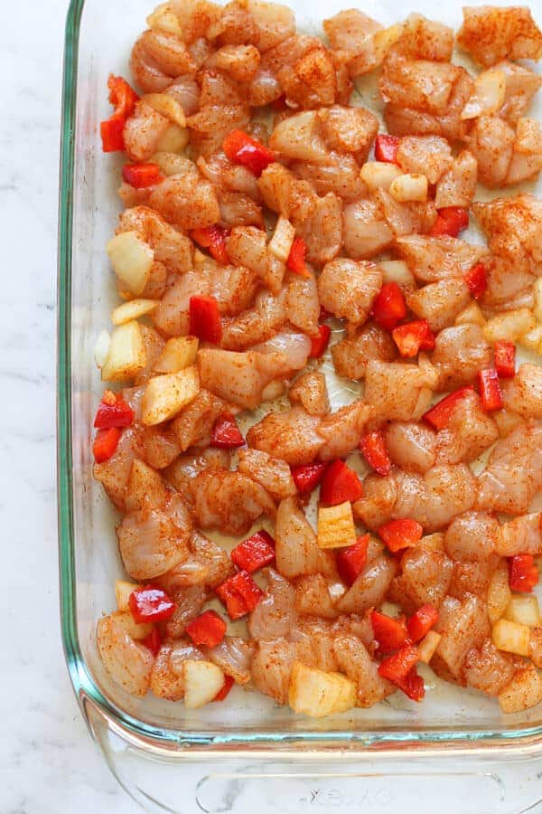 diced raw chicken, onion and capsicum pieces on a baking tray