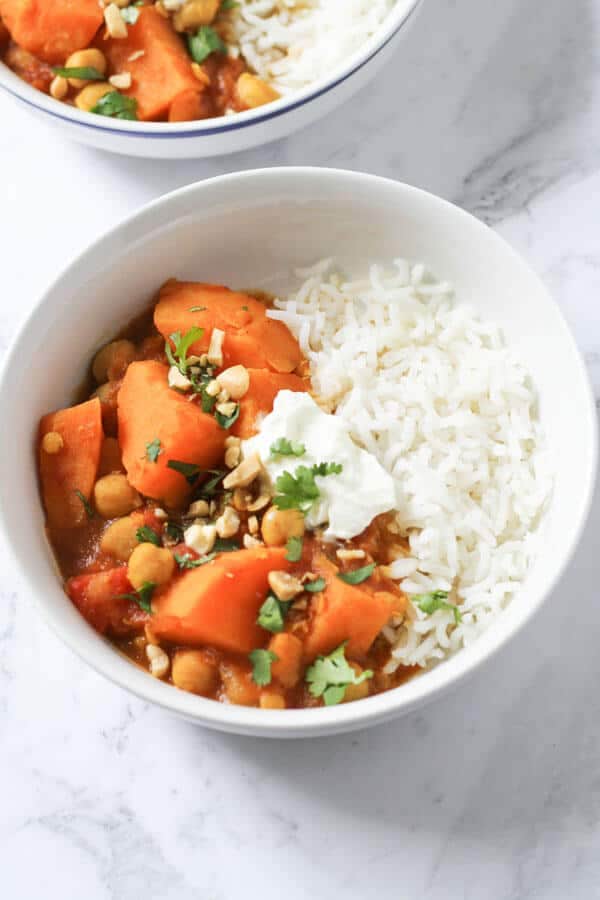 a bowl of sweet potato, lentil & chickpea curry topped with coriander, yoghurt and crushed peanuts