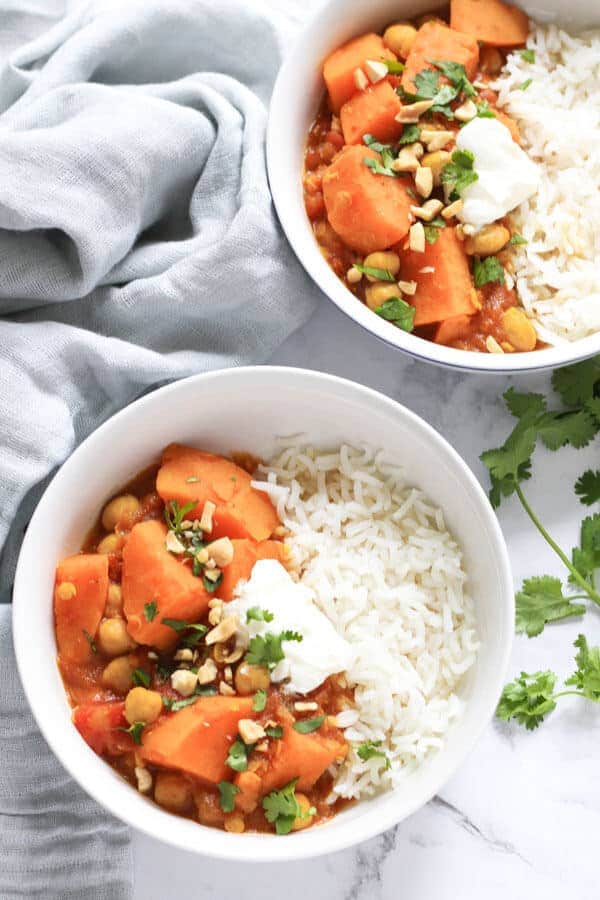 two bowls of sweet potato curry next to a grey napkin and coriander leaves