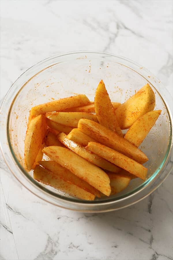 potato wedges in a glass bowl covered in seasoning.