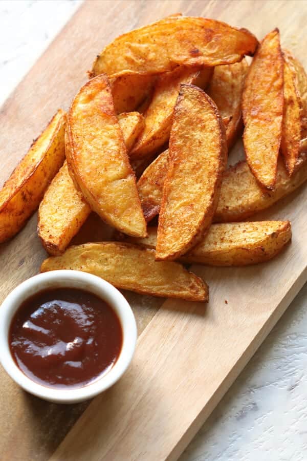 crispy baked potato wedges on a wooden serving board.