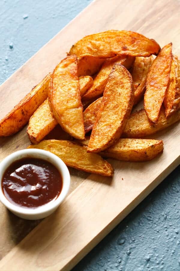 crispy baked potato wedges on a wooden serving board.