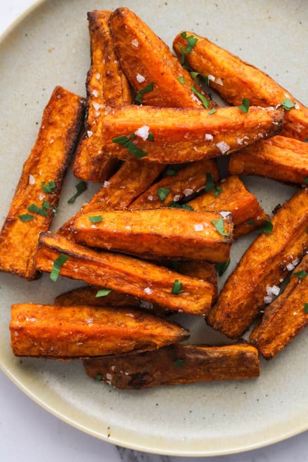 sweet potato wedges covered in salt on a white plate..