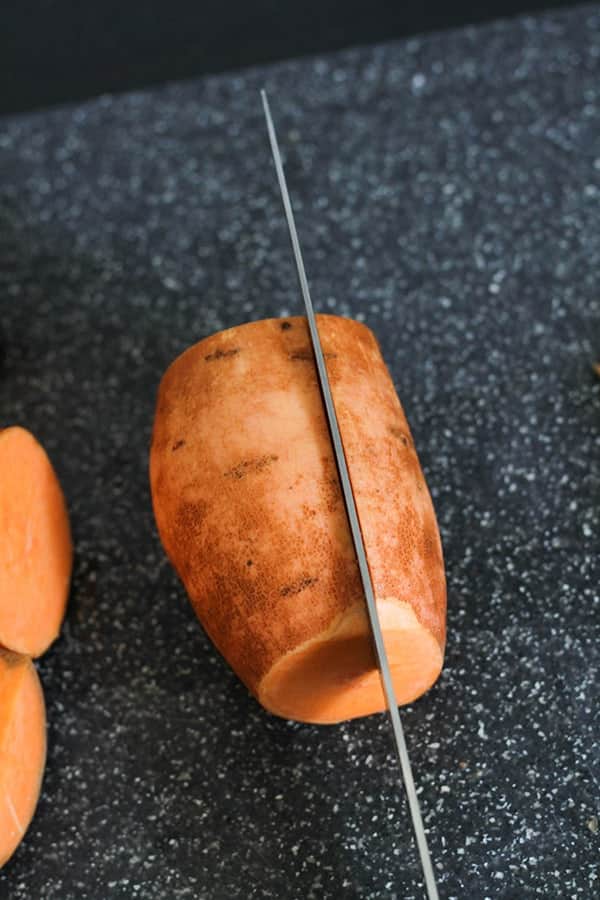 a knife slicing a sweet potato into thirds.