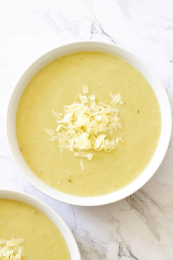 Potato and Leek Soup in a white bowl topped with shredded cheddar cheese.