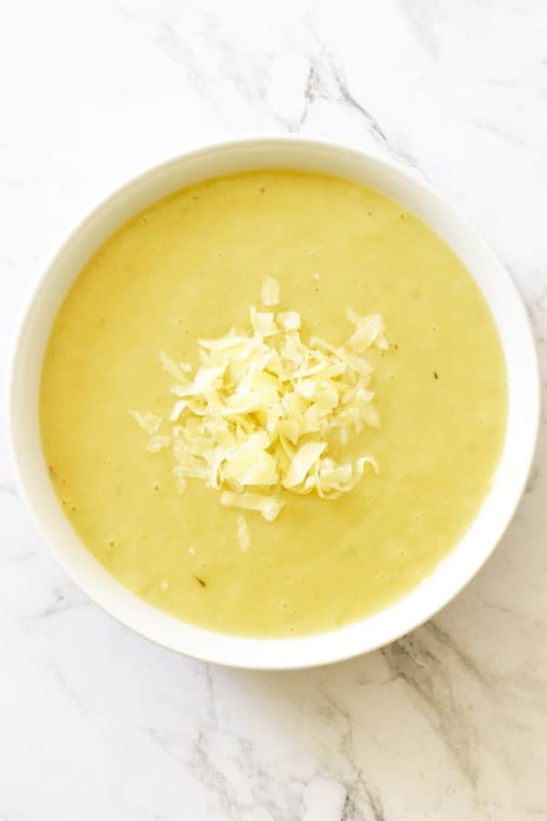 Potato and Leek Soup in a white bowl topped with shredded cheddar cheese.