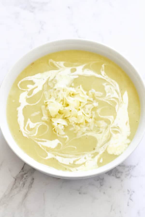 Potato and Leek Soup in a white bowl covered in heavy cream swirls.