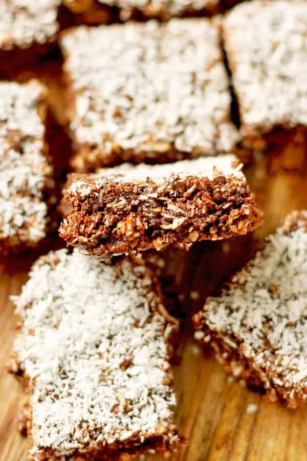 multiple slices of no bake chocolate coconut slice laying on top of a wooden board
