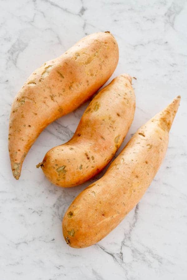 3 sweet potatoes laid on a marble table
