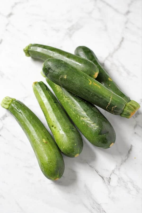 6 zucchinis laying on a white marble background.