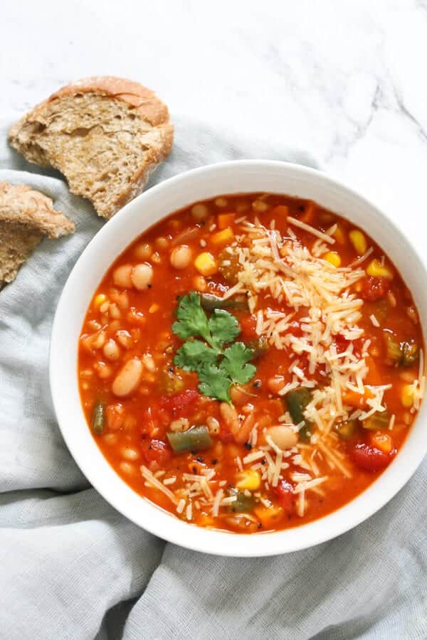 a bowl of vegetable barley soup on a grey napkin with crusty bread
