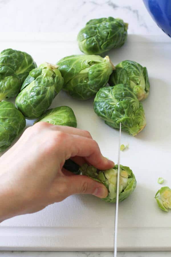 a hand demonstrating how to cut brussels sprouts in half with a knife