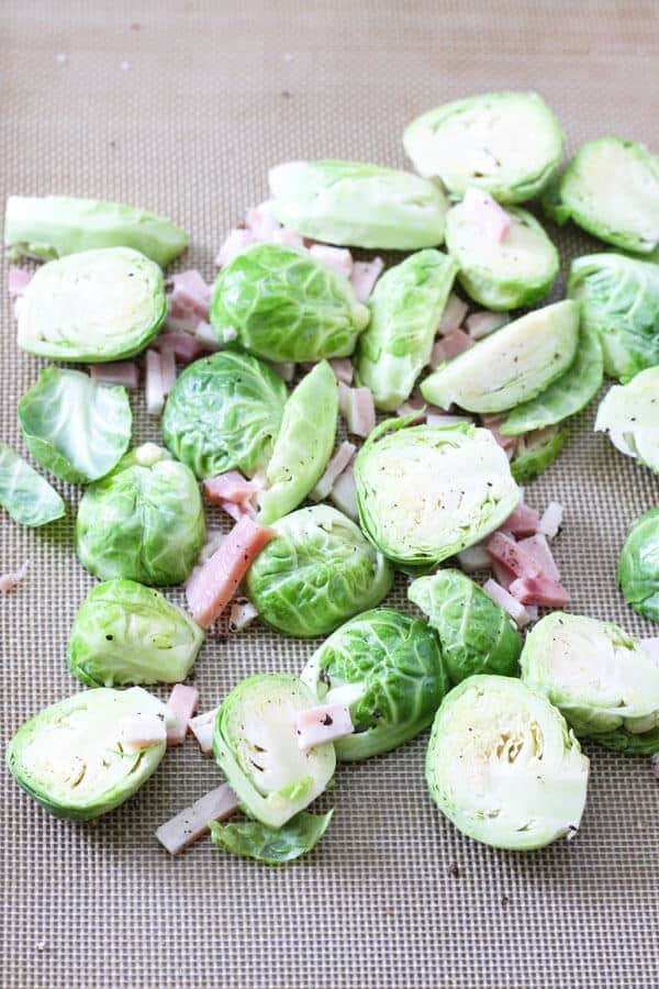 raw trimmed brussels sprouts and diced bacon on a baking tray ready for the oven