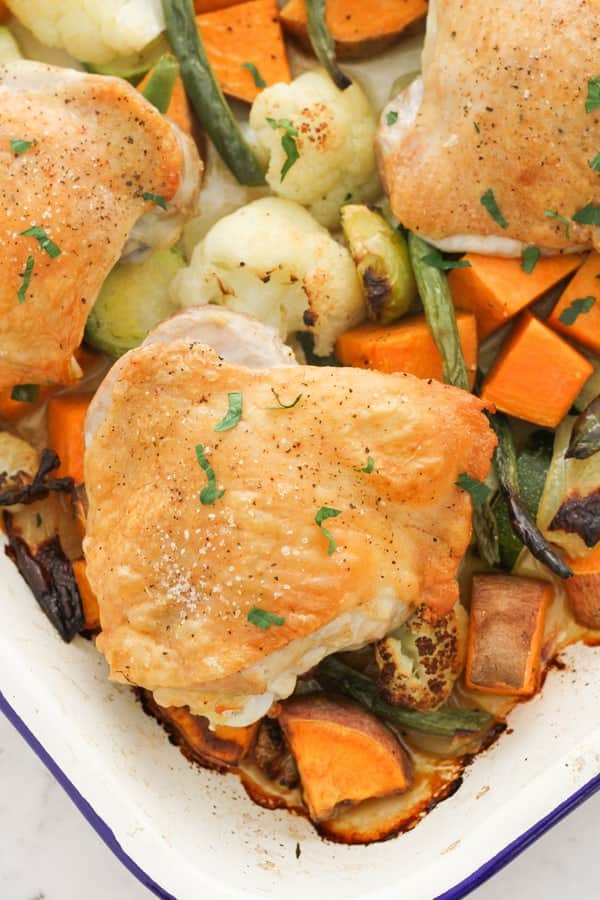 crispy baked chicken thighs on a baking tray with vegetables.