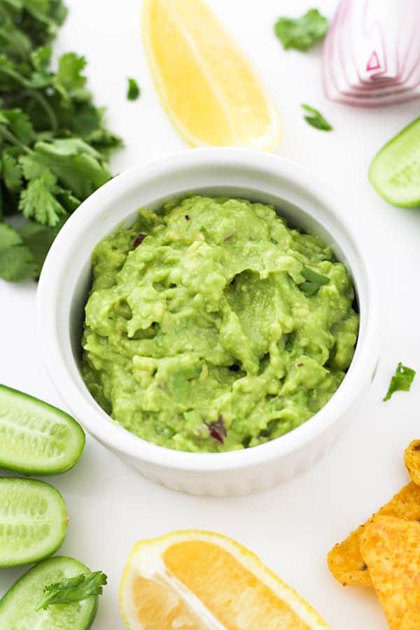 healthy guacamole in a white bowl surrounded by ingredients.